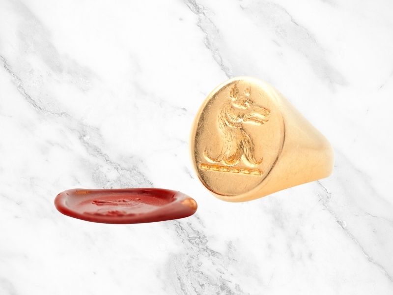 Gold Signet ring with showing an engraving of a wolf and a red was seal.