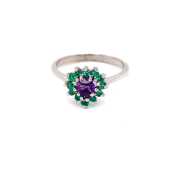 White gold ring with a central purple stone surrounded by green stones in a floral design. The elegant ring reflects luxury and sophistication.