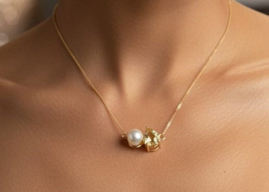 Gold necklace with a pendant featuring a pearl and green gemstone on a person's neck.