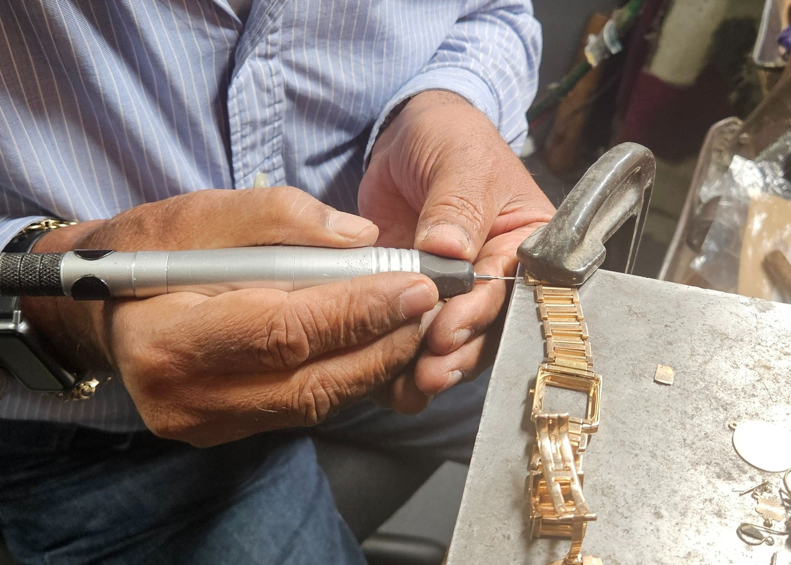 Person working on a gold bracelet with a tool in a workshop setting